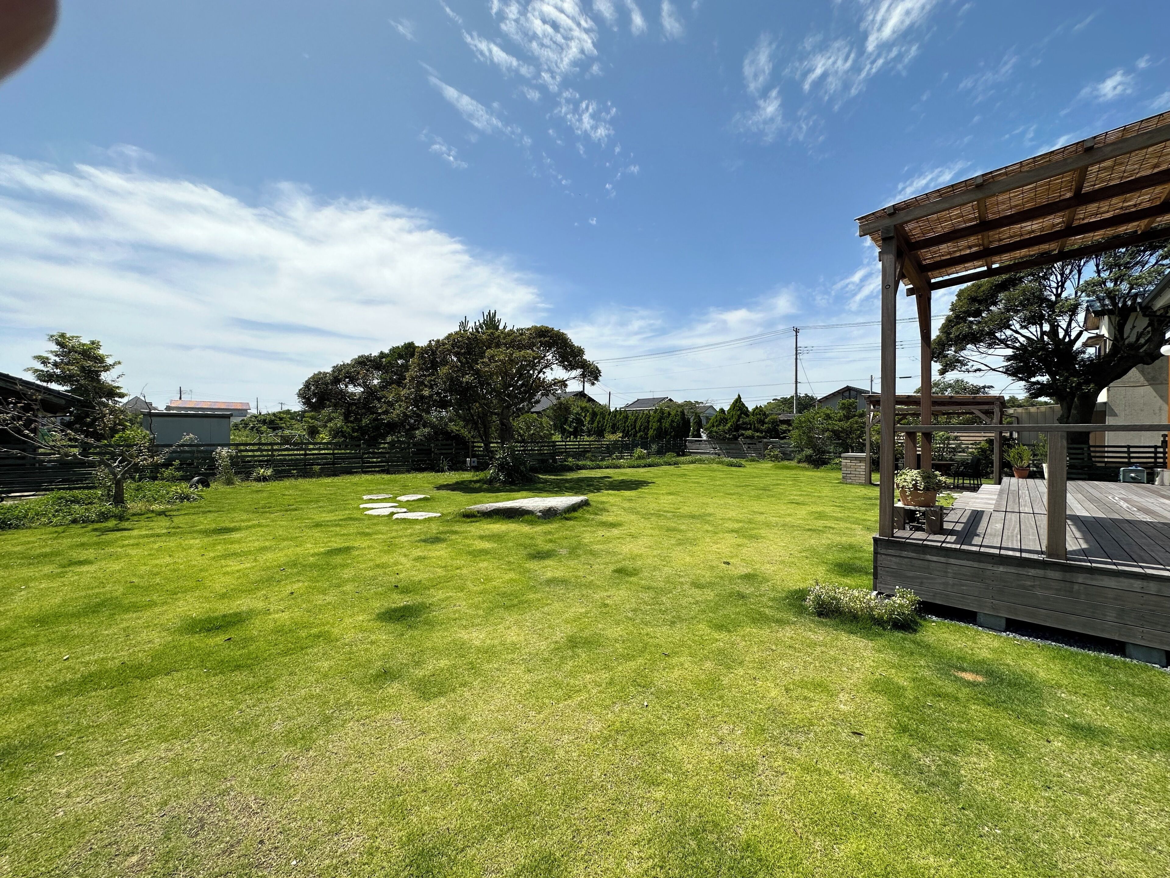 A well-maintained grassy backyard with a wooden pergola, a stone pathway, and a large tree providing shade.