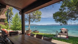 An outdoor dining area with a wooden table and chairs, overlooking a body of water with boats and a distant mountain range. - Peaceful Waters by Hauserman Rentals (Tahoma)