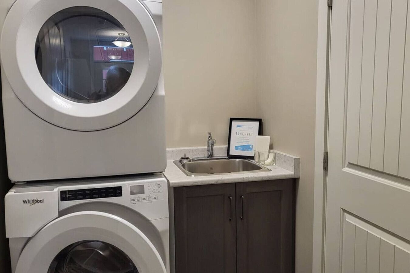 Un espace buanderie compact comprenant un lave-linge Whirlpool à chargement frontal et un évier.