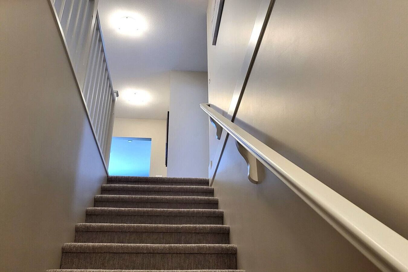 Una escalera empapelada con barandilla, que lleva a un cuarto con una puerta al final.