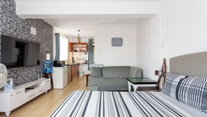 Un espacio habitable compacto con sofá, cama, televisor, kitchenette y comedor.