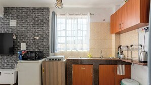 Una cocina compacta con un salpicadero de ladrillo negro, armarios de madera, un refrigerador blanco, un microondas, una estufa y un lavaplatos.