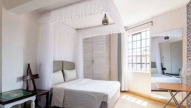 Un dormitorio con cama, escritorio, silla, ventilador y ventana con cortinas.