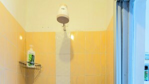 Un baño con baldosas amarillas, un cabezal de ducha, un dispensador de jabón y un perchero para toallas.