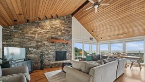 Un salón con chimenea de piedra, techo de madera y un ventanal con vistas panorámicas.