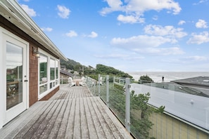 A wooden deck with outdoor furniture, a glass balustrade, and a view of the sea.