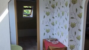 Una habitación con piso de baldosas, una pequeña mesa con mantel rojo y una pared decorativa con diseño de hojas.