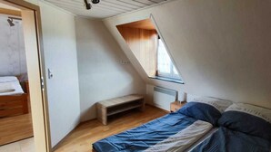Un dormitorio con techo inclinado, una cama, un pequeño banco y una ventana.