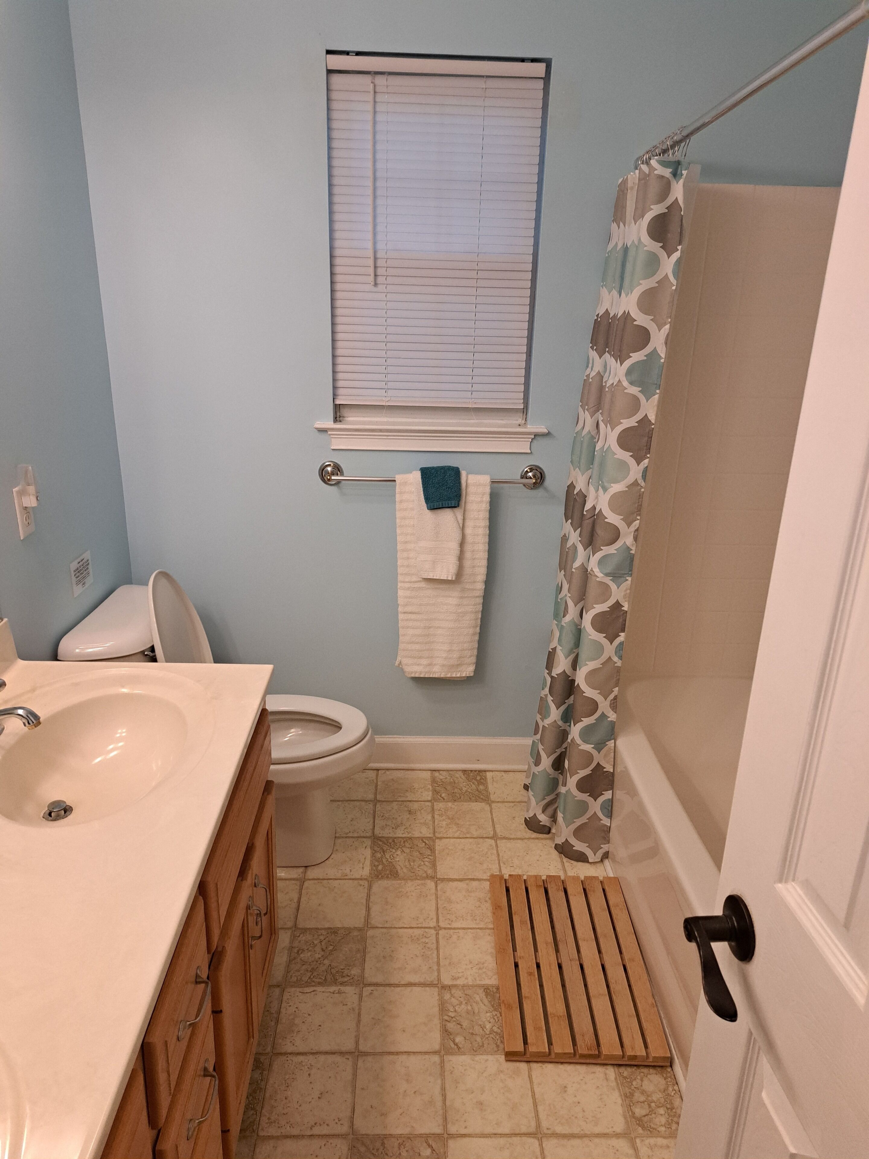 A bathroom with a sink, toilet, window, shower curtain, and a towel rack.