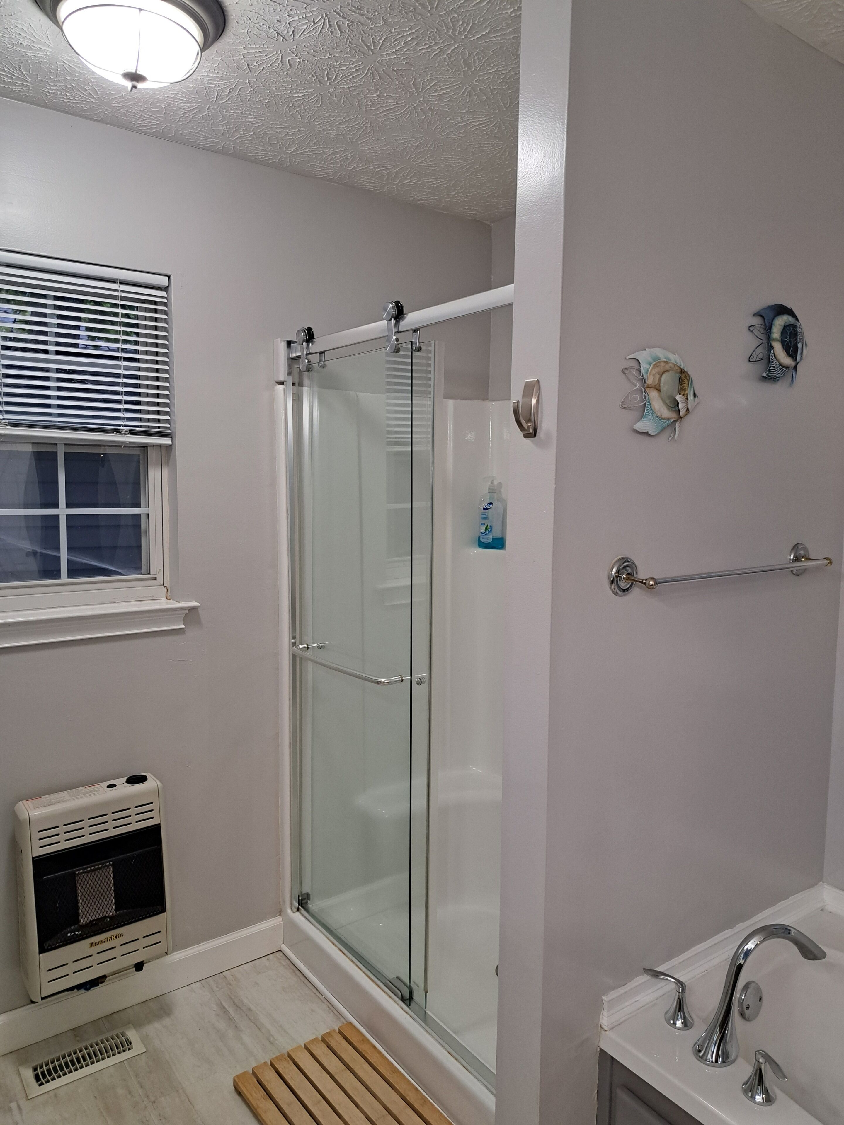 A bathroom with a glass shower enclosure, a white sink with a chrome faucet, and a window with blinds.