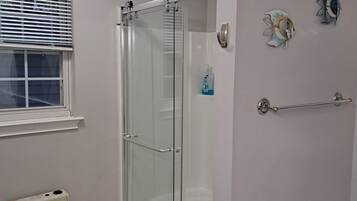 A bathroom with a glass shower enclosure, a white sink with a chrome faucet, and a window with blinds.