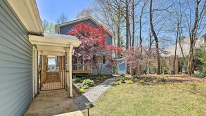 A residential property with a covered porch, a small deck, and a well-maintained garden with various plants and a tree with red foliage.