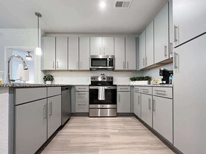 A modern kitchen with stainless steel appliances, grey cabinetry, and a wooden floor.