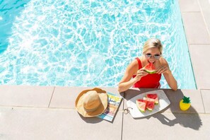 A poolside setting with a magazine, a hat, and watermelon slices on a tray.