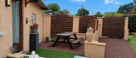 A patio area with a wooden table and benches, surrounded by a low wall and a garden.