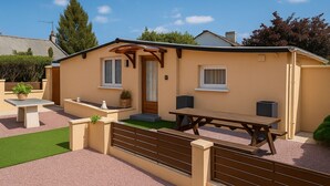 A single-story house with a patio, a wooden table, and a bench.