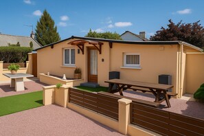 A single-story house with a patio, a wooden table, and a bench.