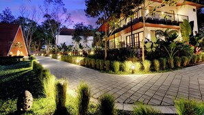 A two-story building with a balcony, surrounded by lush greenery and a paved walkway. - Sandesh Water Edge Kabini  (Heggadadevankote)