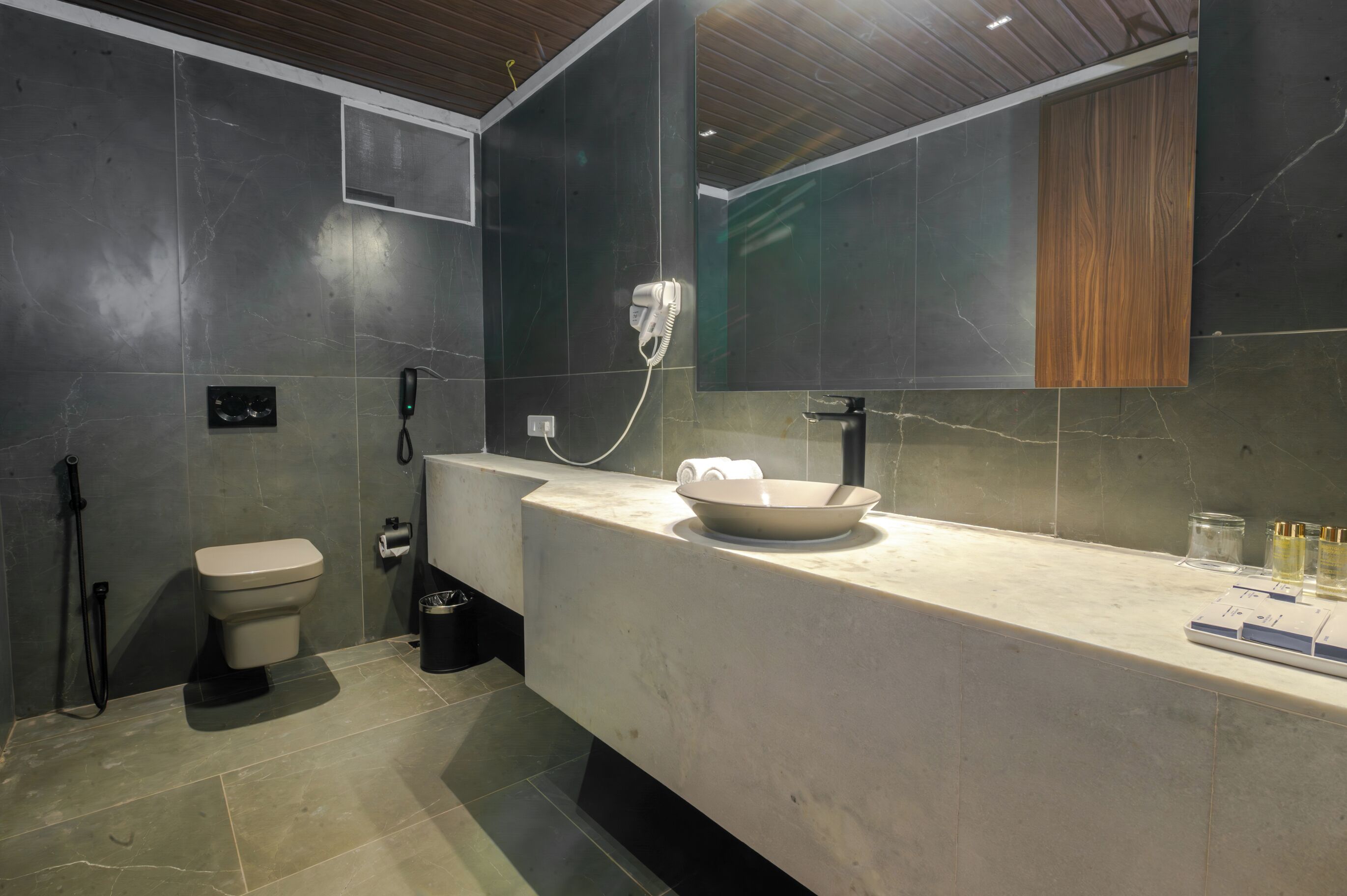 A modern bathroom with a marble sink, a hairdryer, a toilet, and a mirror.