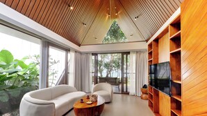 A modern living room with a wooden ceiling, large windows, a sofa, a coffee table, and a TV. - Sandesh Water Edge Kabini  (Heggadadevankote)