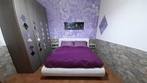 A bedroom with a bed, a wardrobe, a nightstand, and a wall-mounted picture.