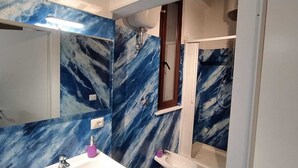 A bathroom with blue marble walls, a large mirror, a sink, and a shower area.