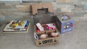 A wooden box labeled "COFFEE" with various items including a newspaper, a mesh container, and a box of Tisa Nite.