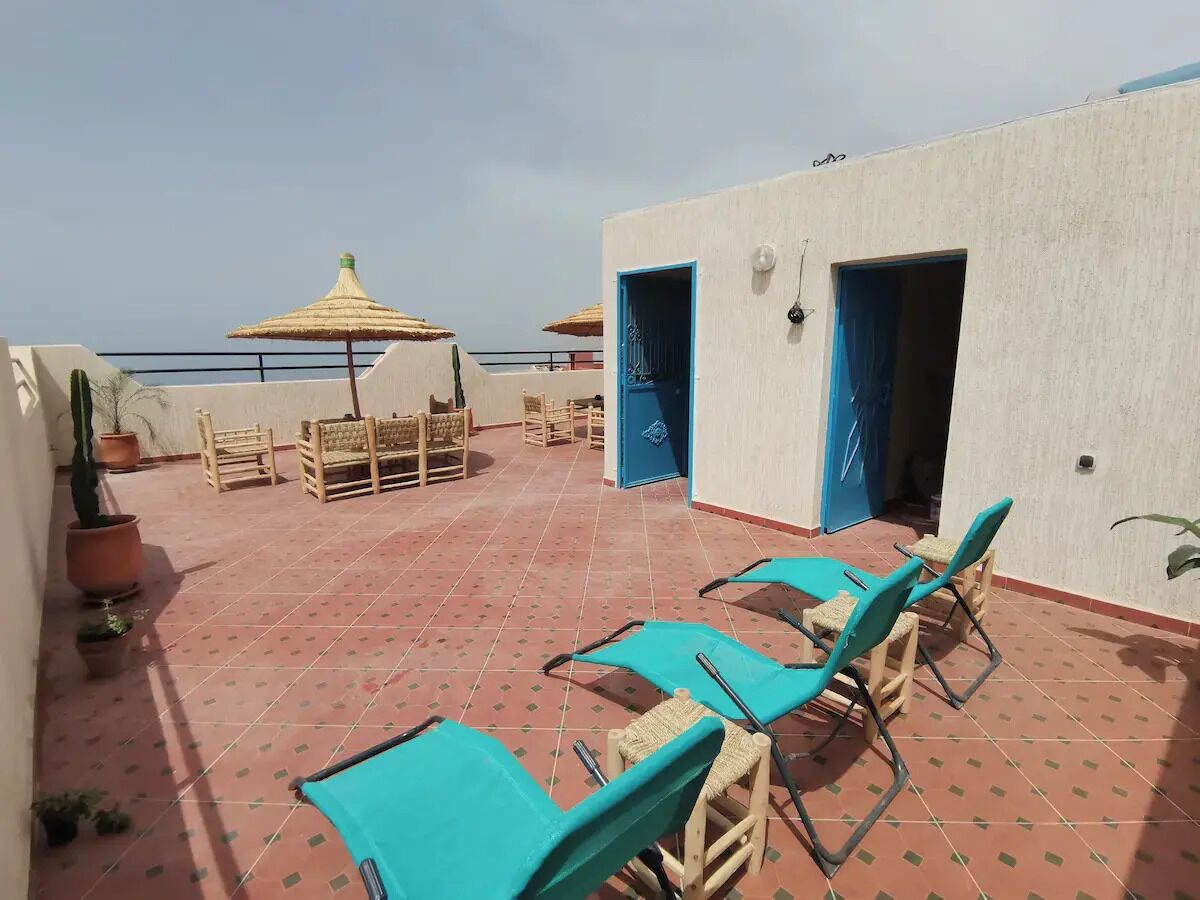 A rooftop terrace with several lounge chairs and a table, a small umbrella, and a potted plant.