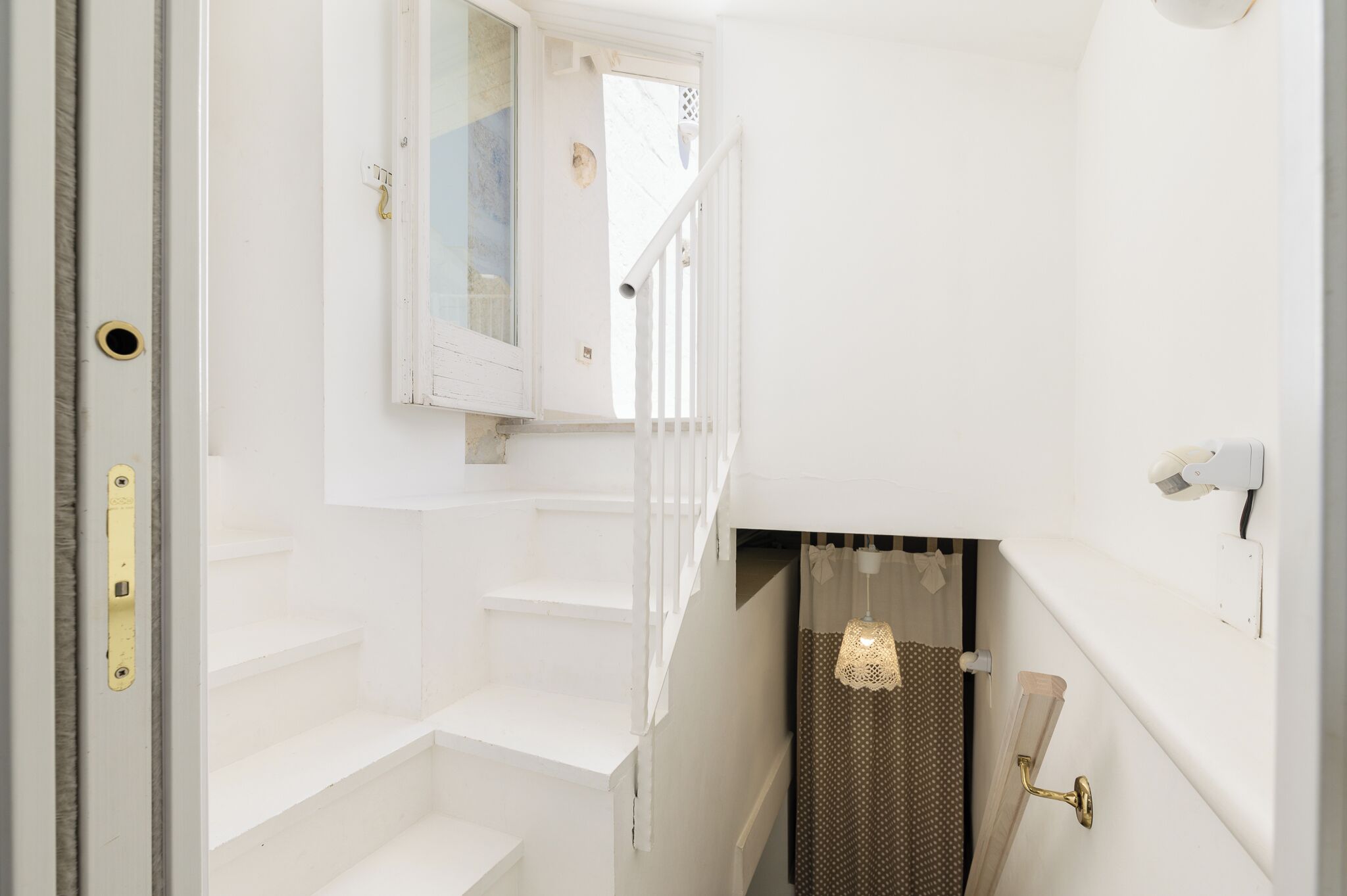 A staircase with white walls and a door leading to a room with a window and a curtain.
