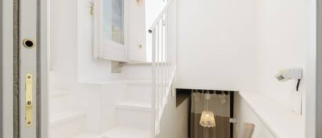Una escalera con paredes blancas y una puerta que da a una habitación con ventana y cortina.