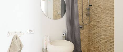 A bathroom with a round sink, a mirror, a towel rack, and a shower with a brick wall backdrop.