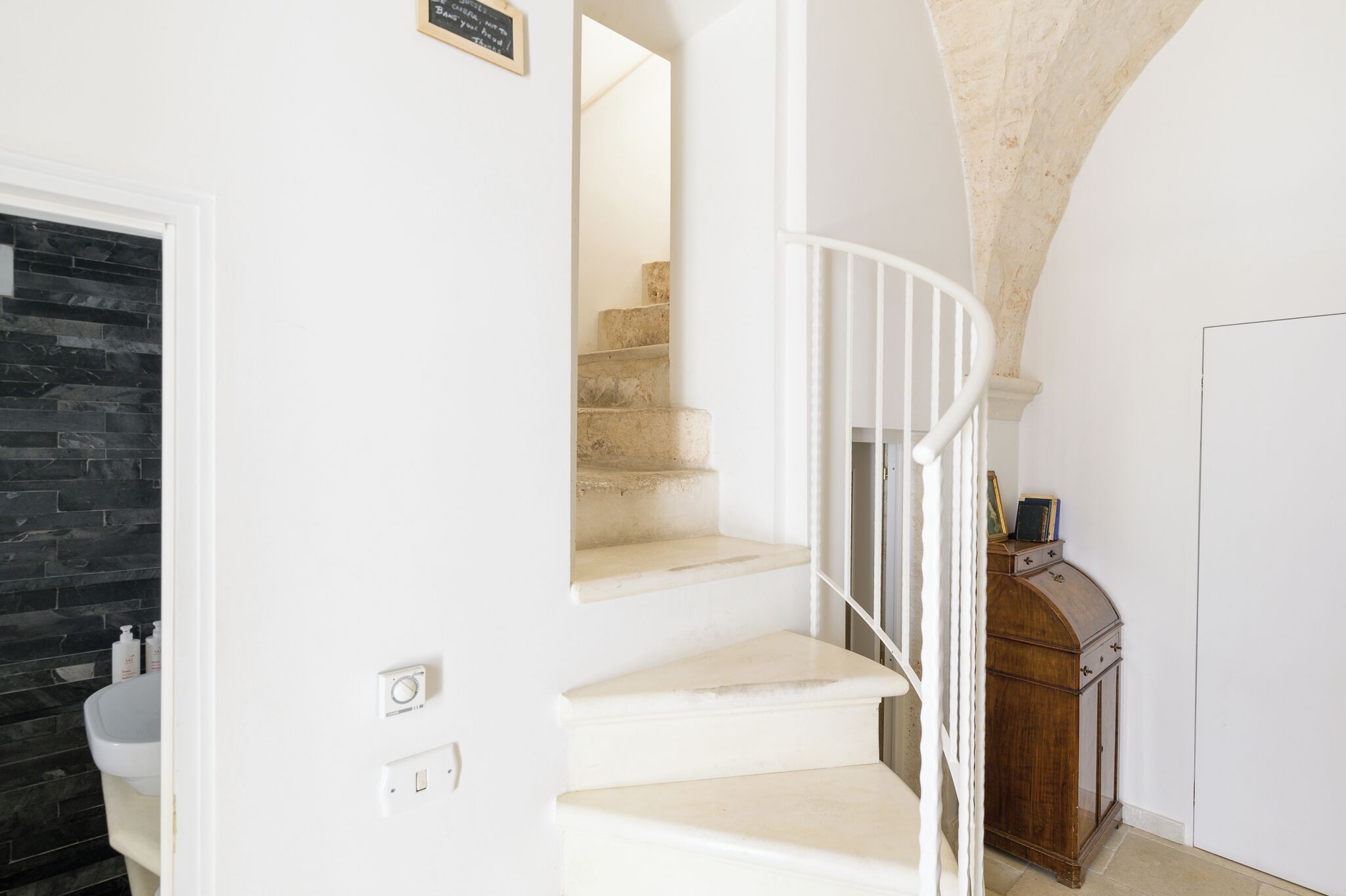 A staircase with white railings, a stone wall, and a wooden cabinet.