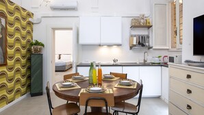 A modern kitchen with white cabinets, a dining table set for four, and a TV mounted on the wall. - Banchi al Patio - Castel Sant Angelo (Rome)
