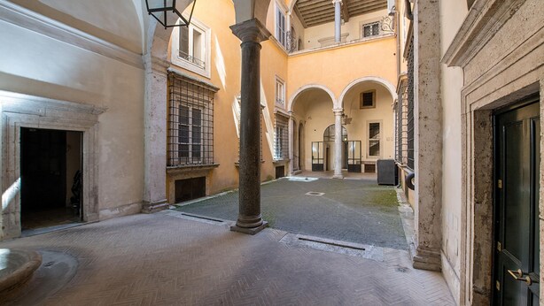 A courtyard with a fountain, columns, and a door. - Banchi al Patio - Castel Sant Angelo (Rome)