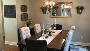 A dining room with a dark wooden table, cushioned chairs, a chandelier, and decorative wall art. - Saratoga Racetrack and SPAC getaway  (Saratoga Springs)