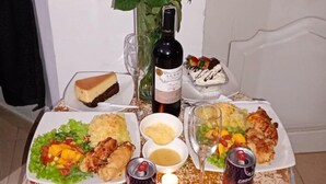 A table set with a bottle of wine, a vase of red roses, and various dishes including a cheesecake, a can of Coca-Cola, and a dessert. - Hostel VIM (Cartagena)