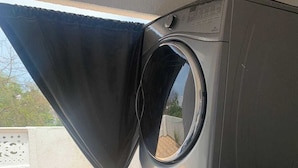 A compact, modern laundry room with a large washing machine and dryer stacked together. - Hostel VIM (Cartagena)