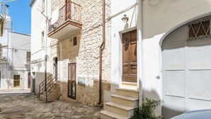 A narrow cobblestone street with a white building featuring a wooden door and a small set of steps leading to a balcony.