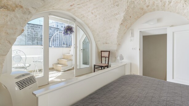 A bedroom with a curved ceiling, a large window, a bed, a chair, and a radiator.