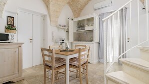 A dining area with a wooden table and chairs, a kitchen with white cabinets, and a staircase with a white railing.