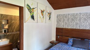 Une chambre à coucher comprenant un lit, une table de chevet, un miroir et un mur orné de trois tableaux représentant des oiseaux.