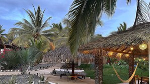 Un jardin tropical avec des palmiers, un kiosque à toit de chaume et un banc en bois.