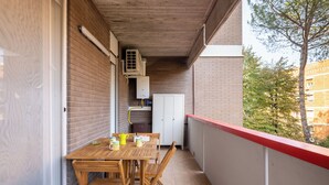 Un balcón con mesa y sillas de madera, un armario blanco y una barandilla roja.