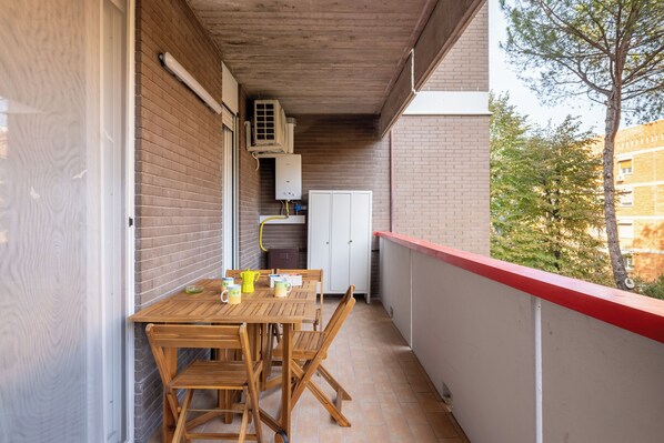A balcony with a wooden table and chairs, a white cabinet, and a red railing.