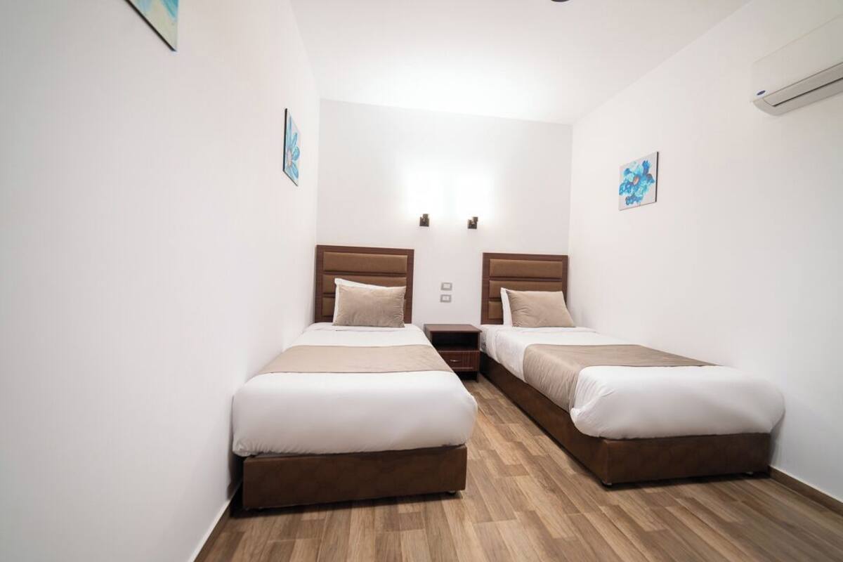 A hotel room with two beds, wooden flooring, and white walls.