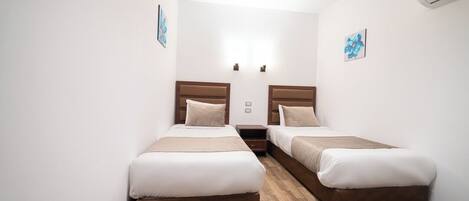 A hotel room with two beds, wooden flooring, and white walls.