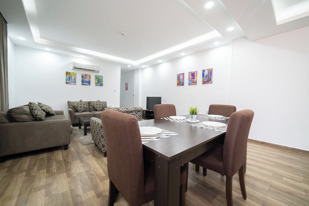 A modern living room with a dining area, featuring a sofa set, a dining table with chairs, and artwork on the walls.