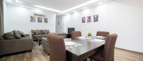 A modern living room with a dining area, featuring a sofa set, a dining table with chairs, and artwork on the walls.