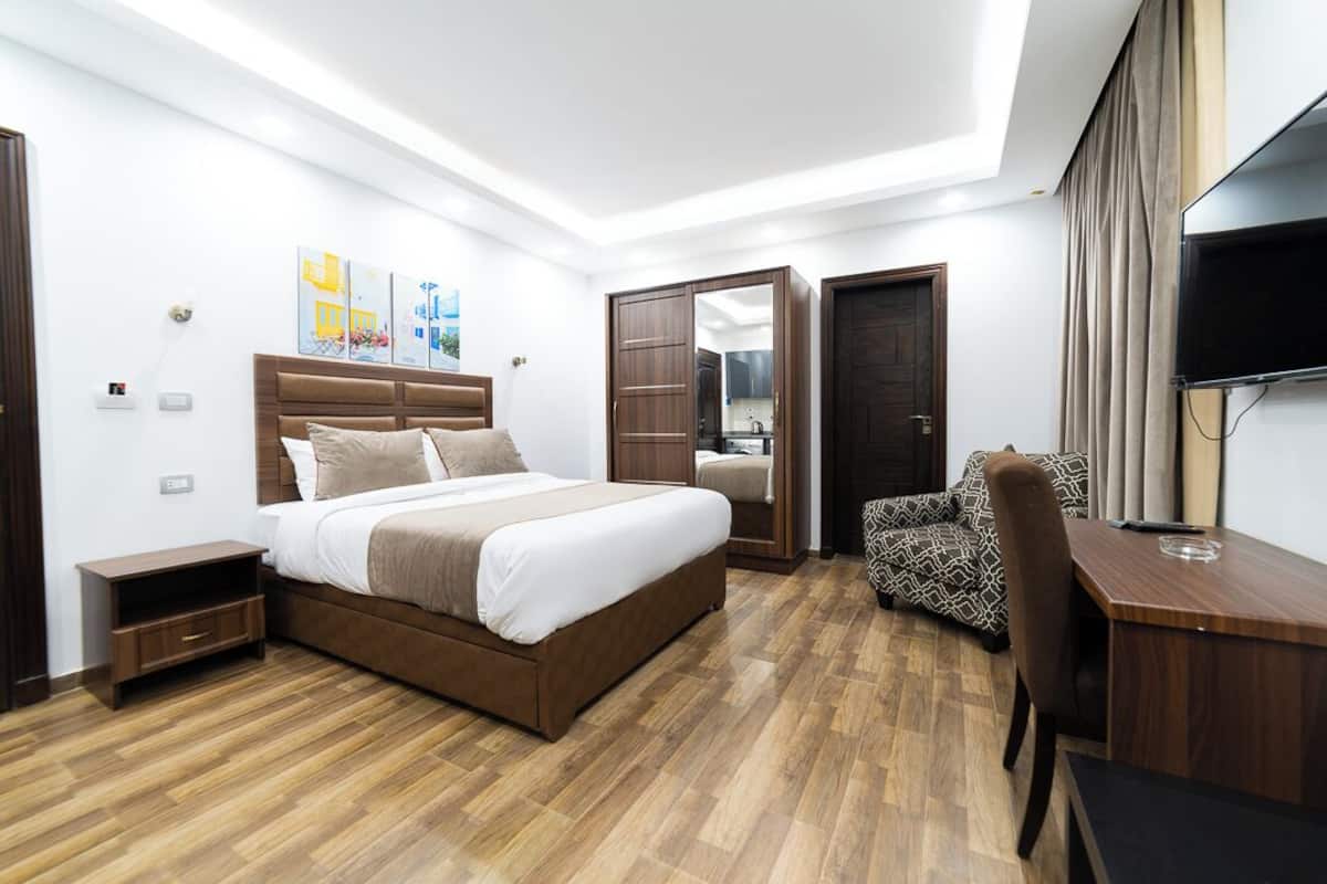 A modern hotel room with a large bed, a desk, a chair, and a TV.