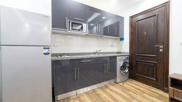 A compact kitchen with a built-in microwave, a washing machine, and dark cabinets.
